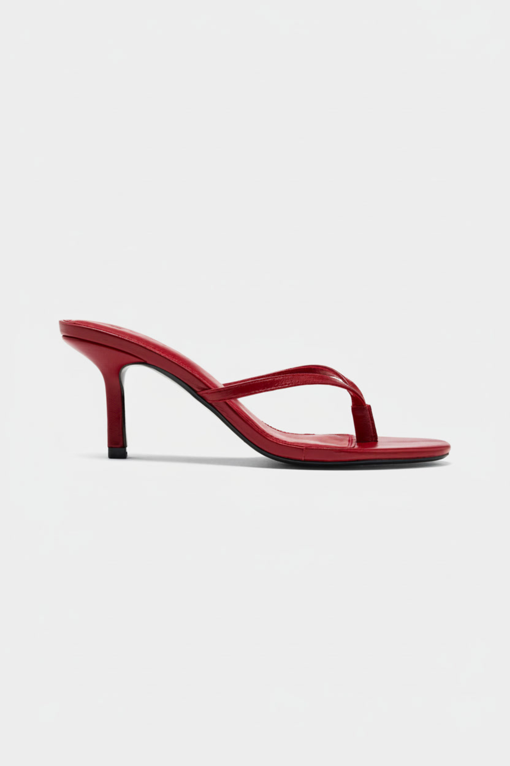 The Realm Spirit Heeled Sandals in red leather feature a thong strap design and slender stiletto heel, shown in profile against a plain white background.