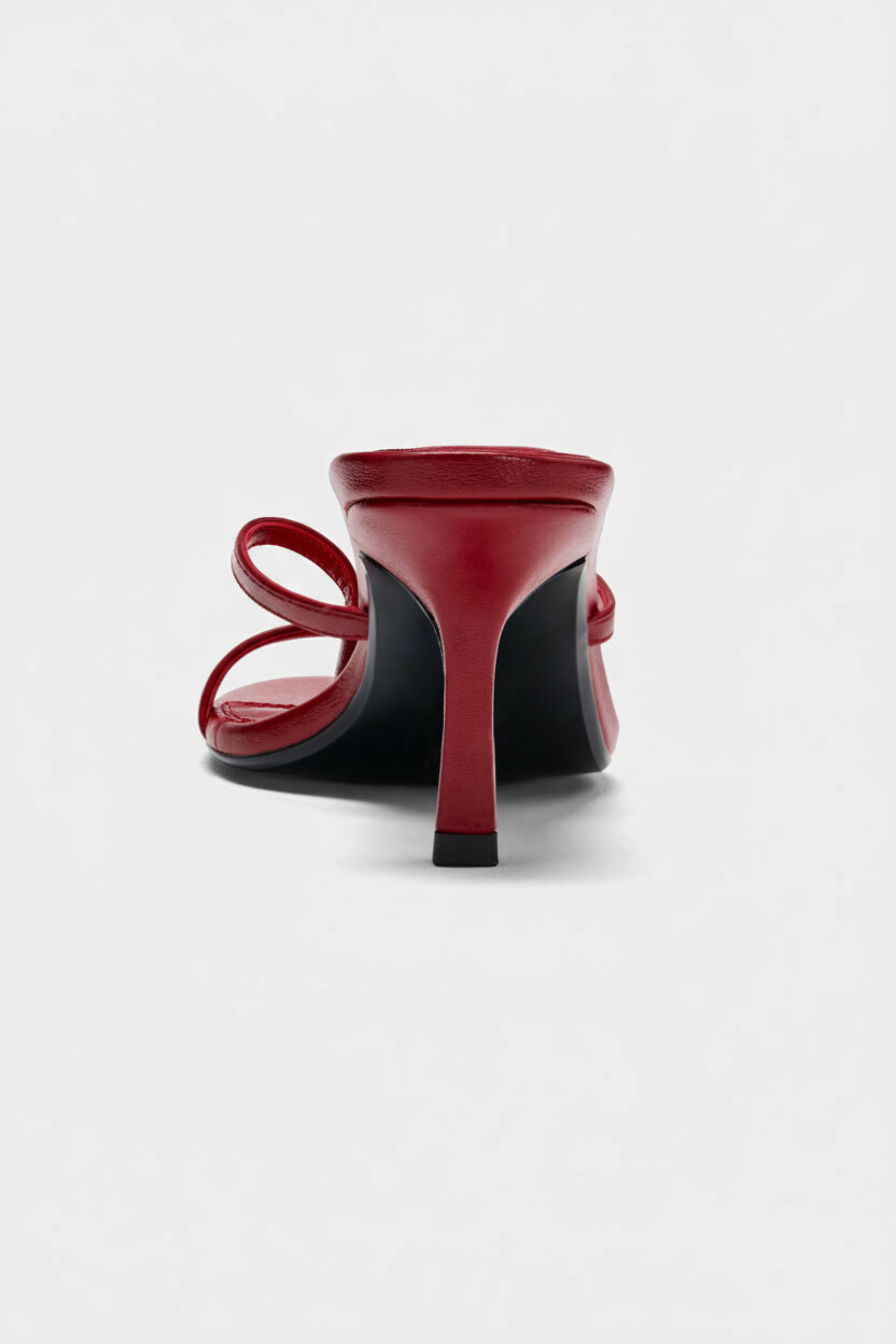 A close-up rear view of the Realm Spirit Heeled Sandals in red leather, featuring an open toe and two slender straps, set against a plain light background.