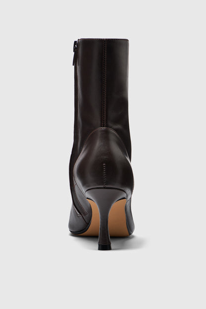 A close-up, rear view of the Realm Encore Ankle Boots in black leather showcases the pointed toe and side zipper on a plain light gray background—an essential piece for any capsule wardrobe.