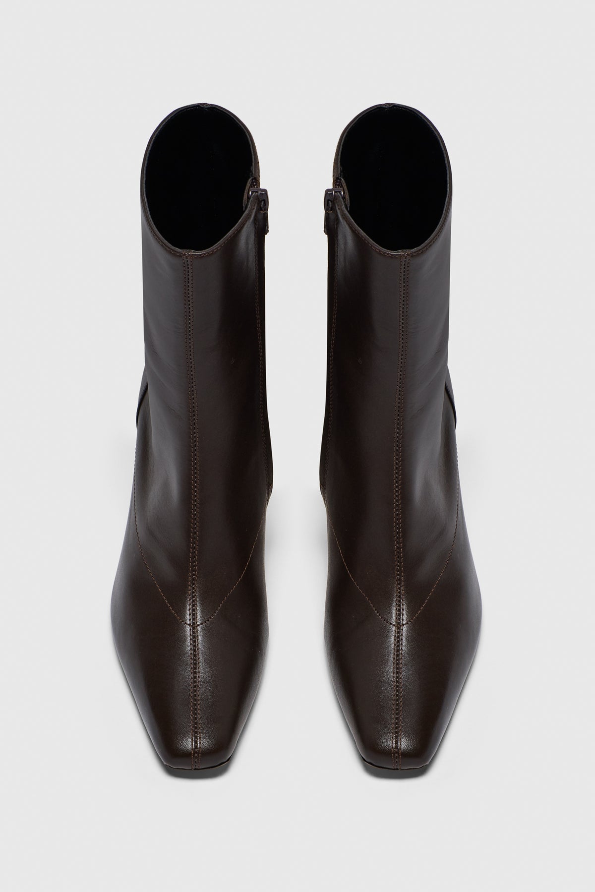The Realm Encore Ankle Boots, crafted from black leather with square toes and visible stitching, are a chic addition to any capsule wardrobe, displayed from above on a light gray background.