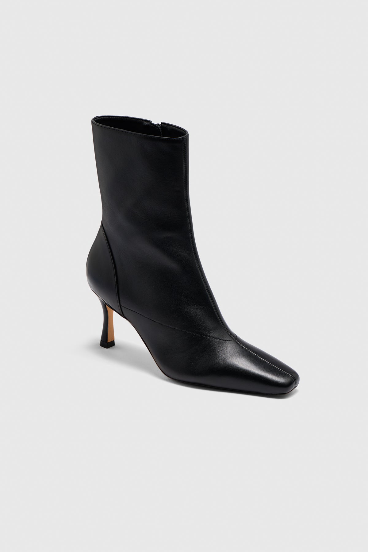 The Realm Encore Ankle Boots—a black leather ankle boot featuring a pointed toe, seam detailing, and a mid-height slender heel—are showcased against a plain light gray background, making them an essential addition to any capsule wardrobe.
