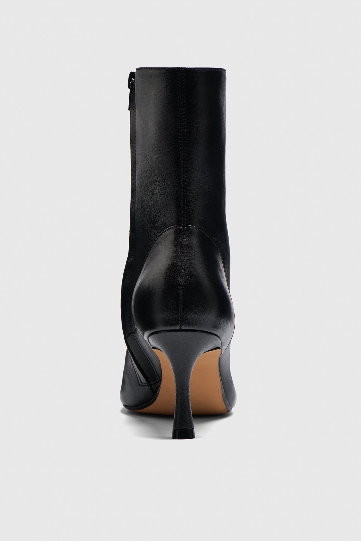 The Boots are featured from the back against a light gray background, showcasing their smooth black leather and slim high heel—a chic addition to any capsule wardrobe.