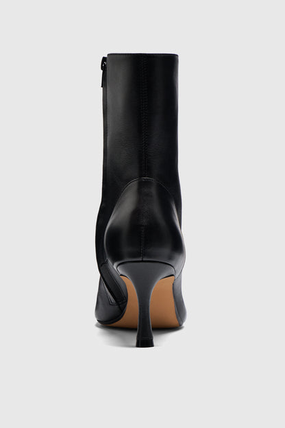 The Boots are featured from the back against a light gray background, showcasing their smooth black leather and slim high heel—a chic addition to any capsule wardrobe.