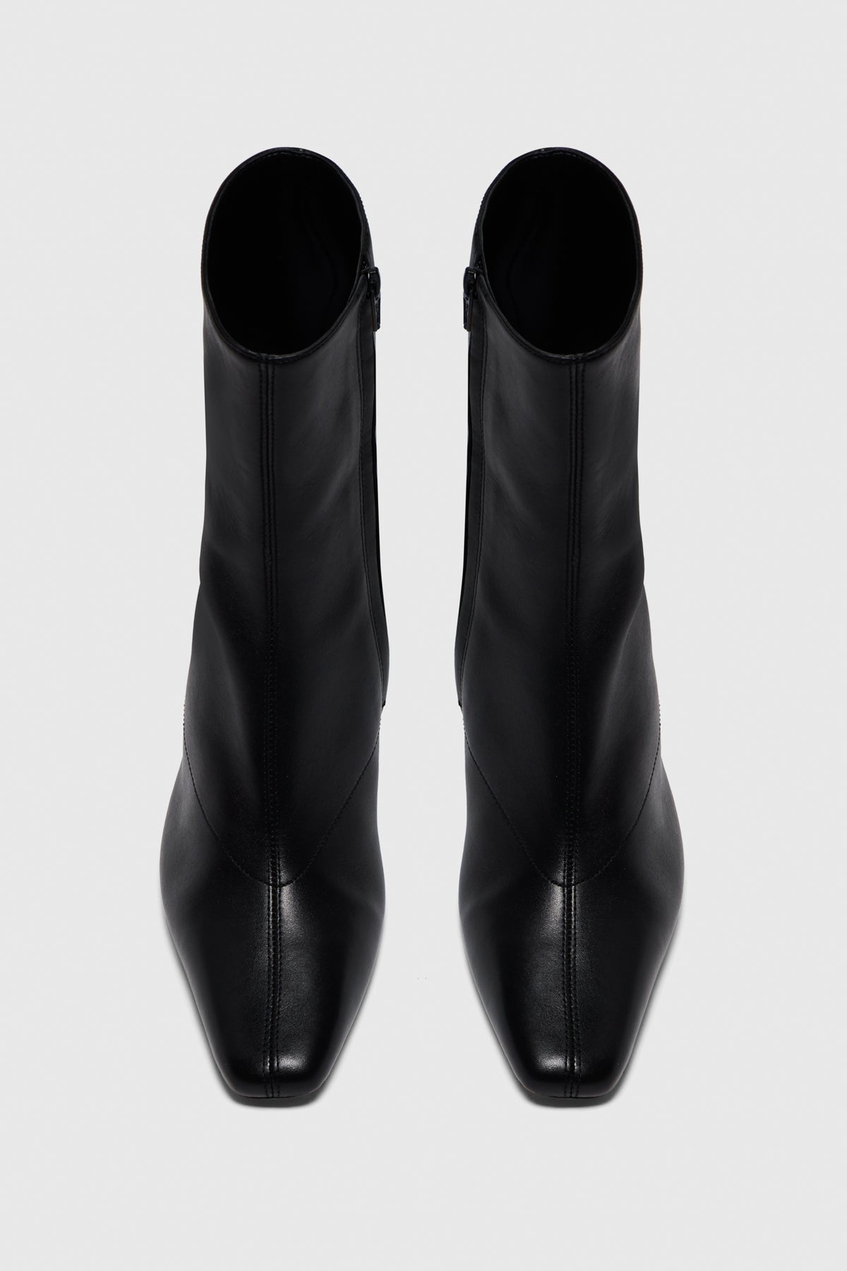 The Boots | Noir Leather by Realm—sleek, black leather high-heeled ankle boots crafted from smooth leather—make an essential addition to any capsule wardrobe, shown from above on a light grey background.