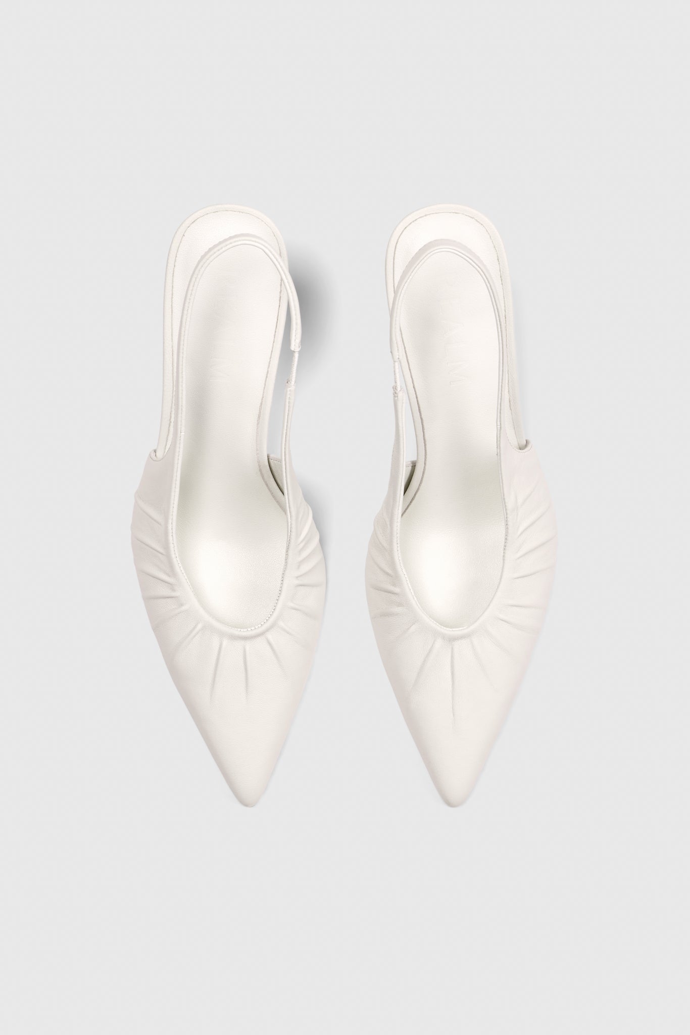 Top view of Realm’s Cascade Slingbacks in white leather—pointed-toe bridal heels with ruched sides—on a light gray background.