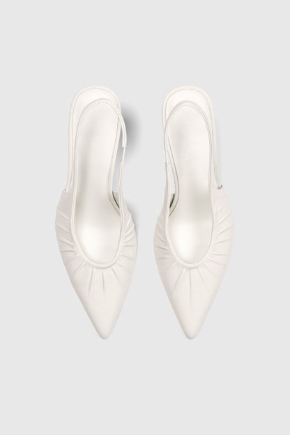 Top view of Realm’s Cascade Slingbacks in white leather—pointed-toe bridal heels with ruched sides—on a light gray background.