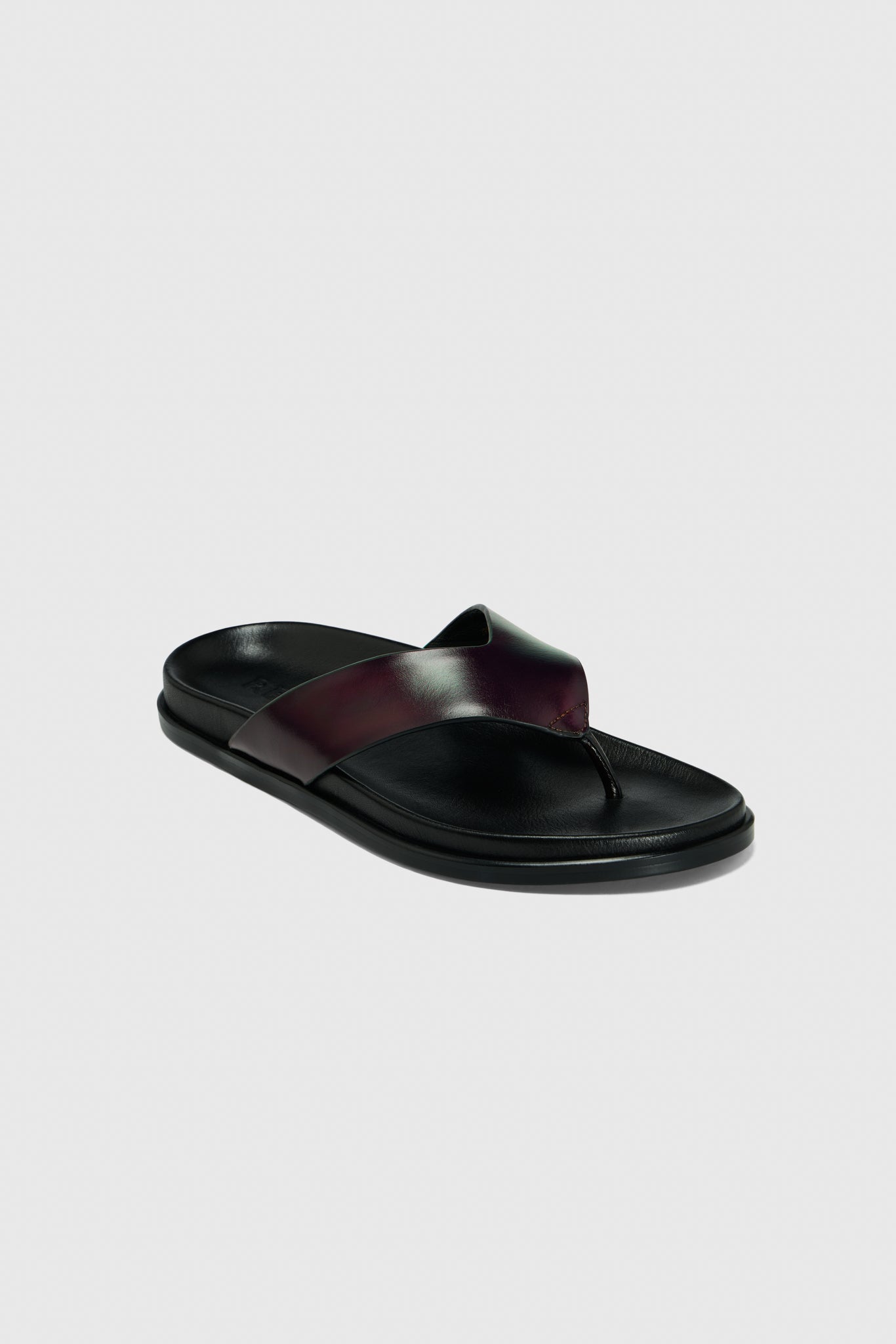 Realm’s Contour Flats in black leather feature wide, crisscrossed leather straps and a contoured footbed, shown on a light gray background.