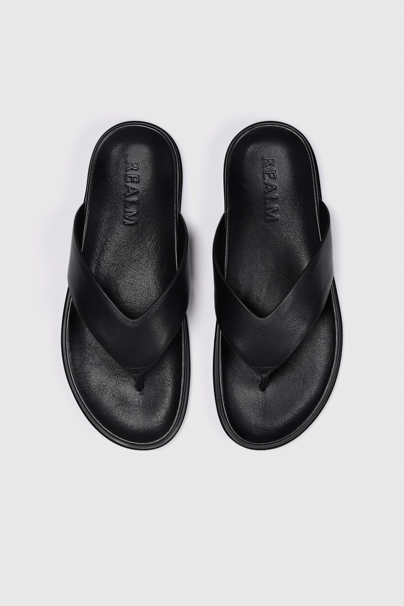 The Contour Flats in black leather by Realm feature wide crisscross straps and a contoured footbed—an effortless slip-on sandal.