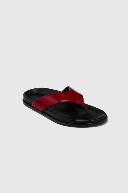 The Realm Contour Flats feature a black leather flip-flop design with a wide, glossy leather thong strap and contoured footbed, set against light gray.
