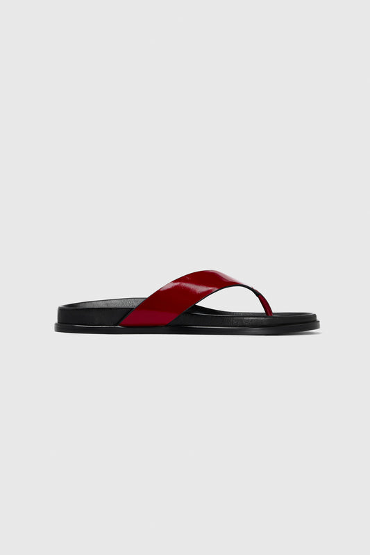 The Realm Contour Flats feature a minimalist modern design with a black sole, contoured footbed, and wide glossy red leather strap.