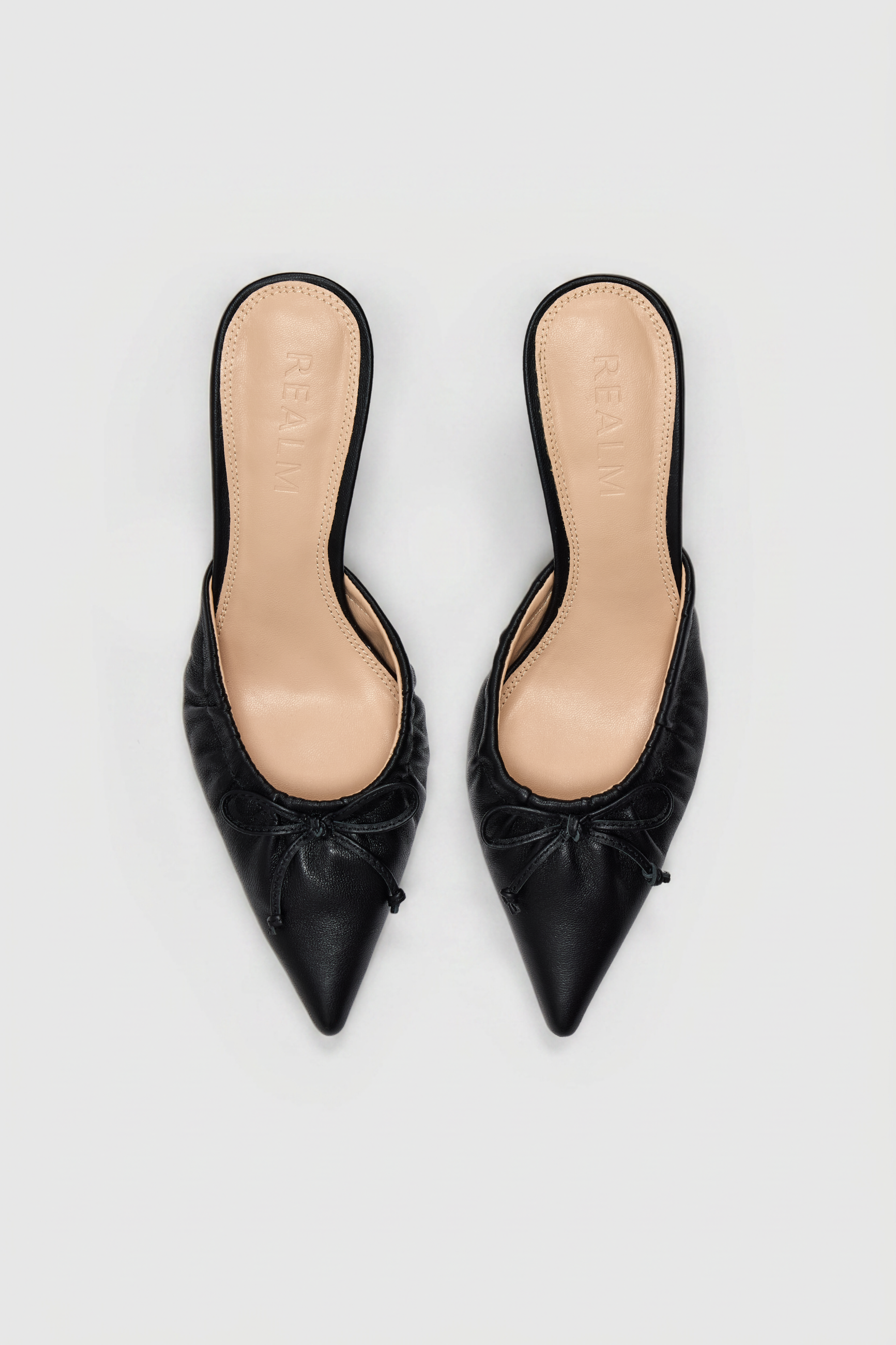 Black leather pointed-toe slip-on mules with gathered detail and small front bows, shown from above on a light background.