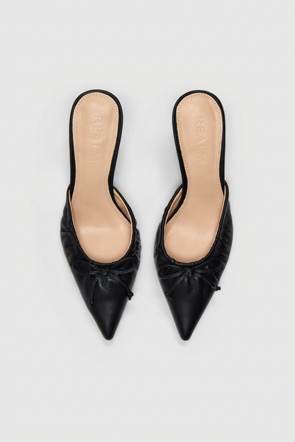 Black leather pointed-toe slip-on mules with gathered detail and small front bows, shown from above on a light background.