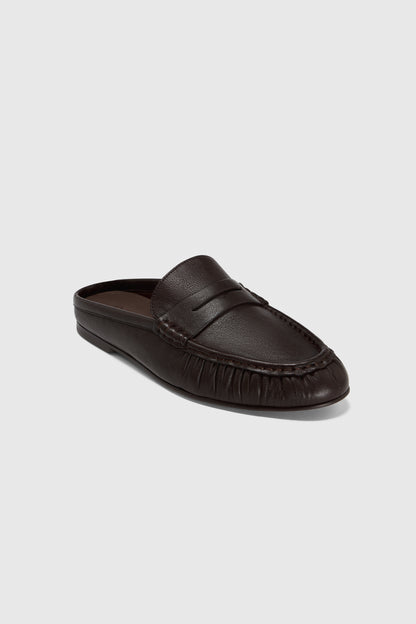 The black leather backless slip-on mules have a low heel, stitched details, and rounded toe, set against a light gray background.