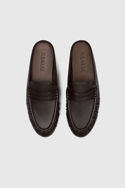 A pair of black leather Realm Everyday Loafers with rounded toes and stitched details are placed side by side on a light gray background. The insoles are embossed with the brand name.