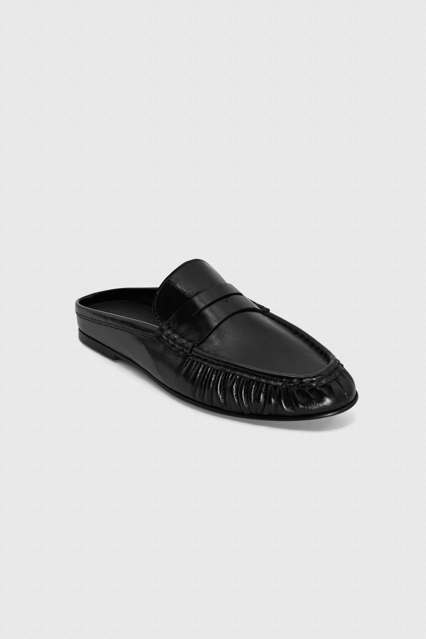 Black leather slip-on mule loafers with penny slot detail and moccasin-style toe stitching, on a plain light gray background.