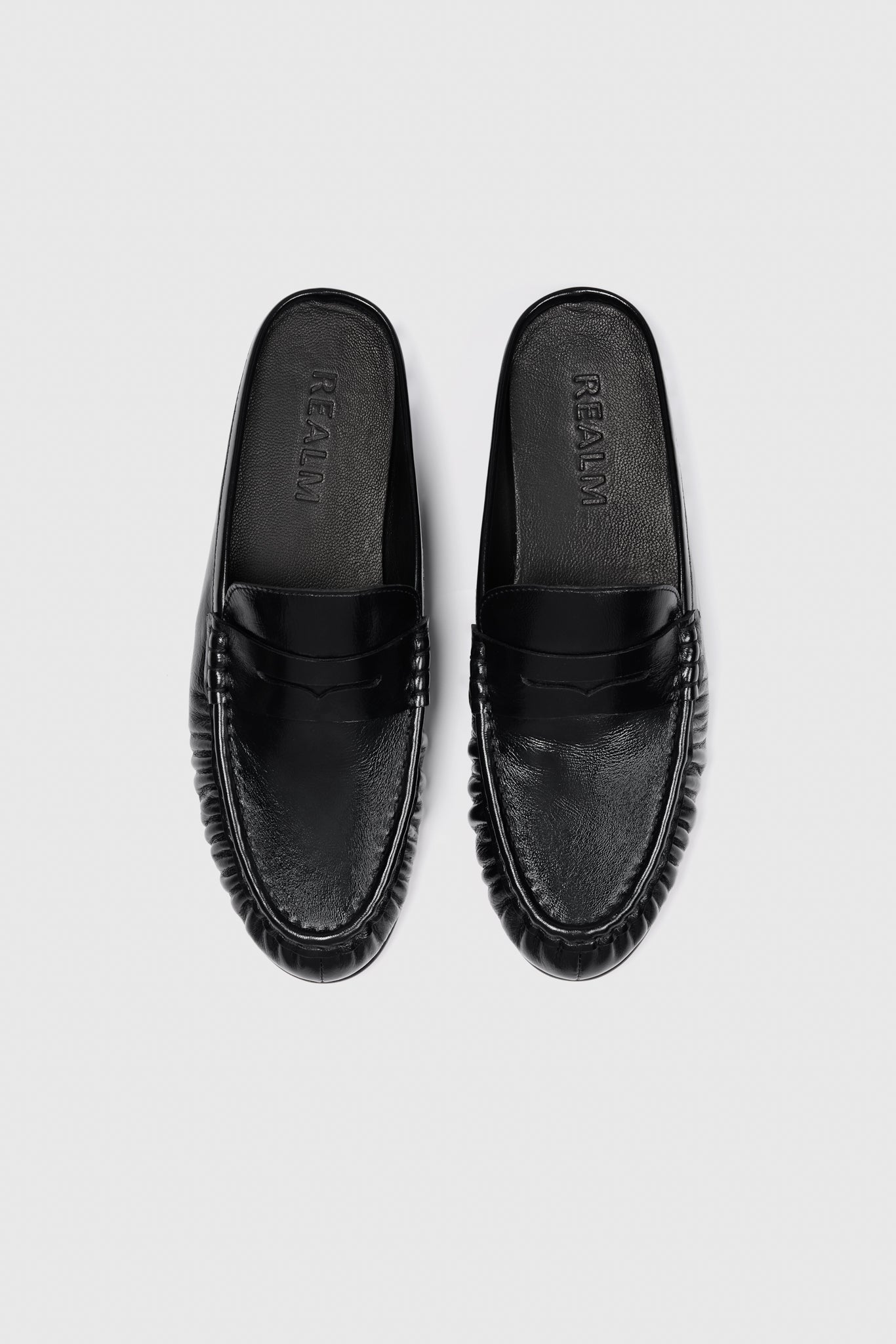 These everyday loafers in black leather feature a sleek slip-on design with rounded toes and textured soles, shown overhead on white.