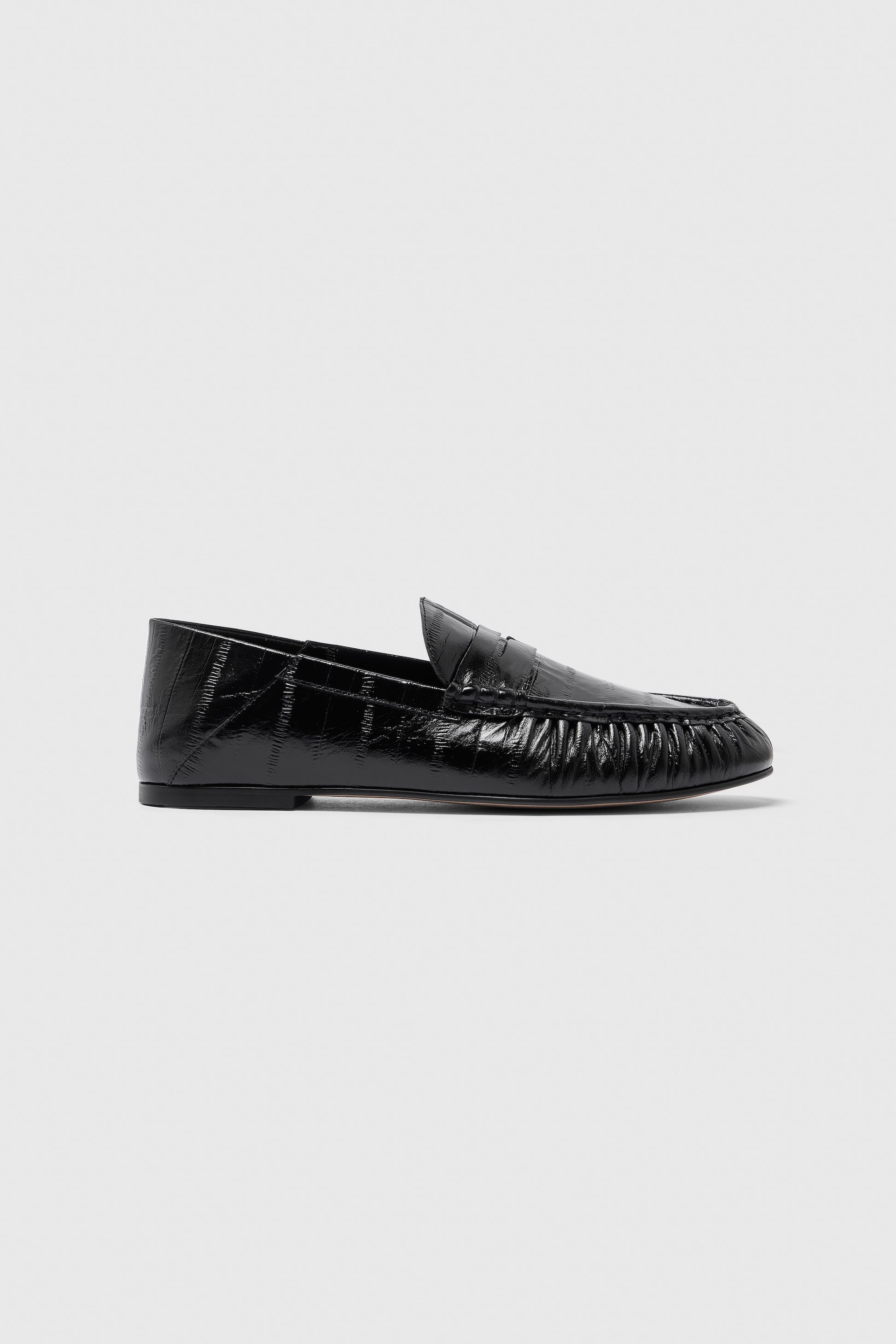 A single Realm Form Loafer | Unagi Leather is shown in profile against a light gray background, highlighting its black embossed leather with a shiny, textured finish, low heel, and slightly rounded toe.