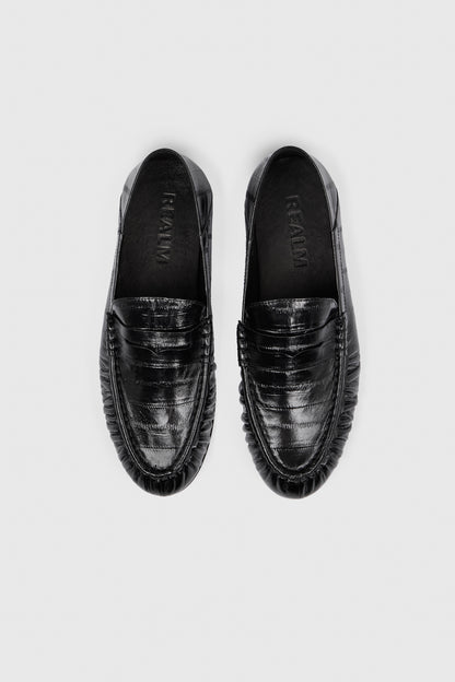 A pair of Realm’s Form Loafers in glossy black leather, shown from above on a light gray background. Embossed leather with toe stitching and the brand name visible inside.
