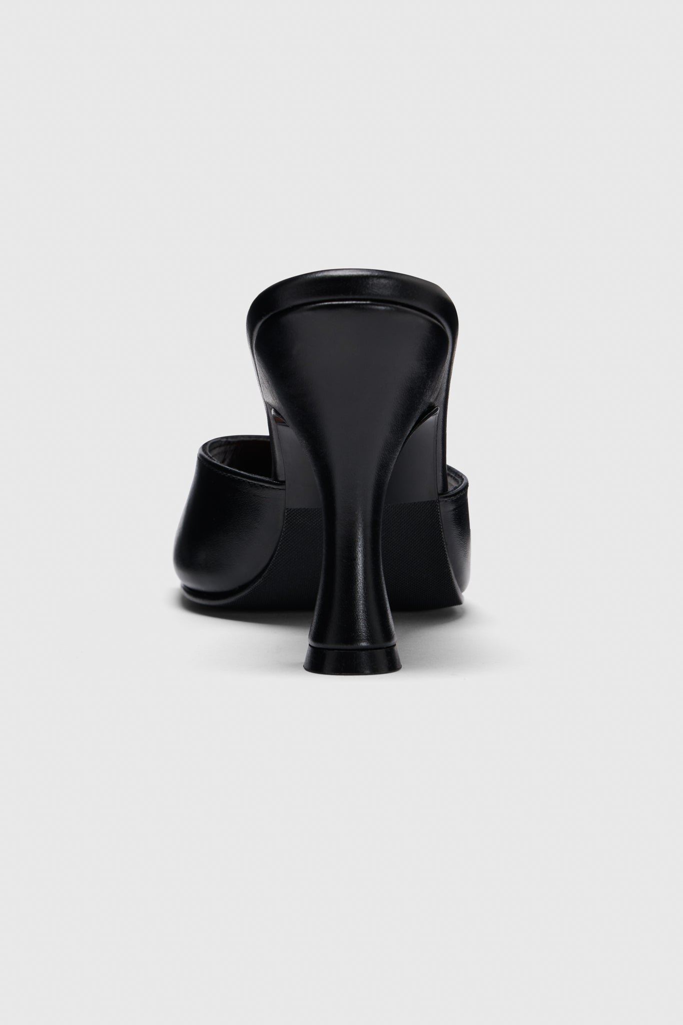 Rear view of black leather mules by Realm, showing their curved heel and closed toe, set against a light gray background.