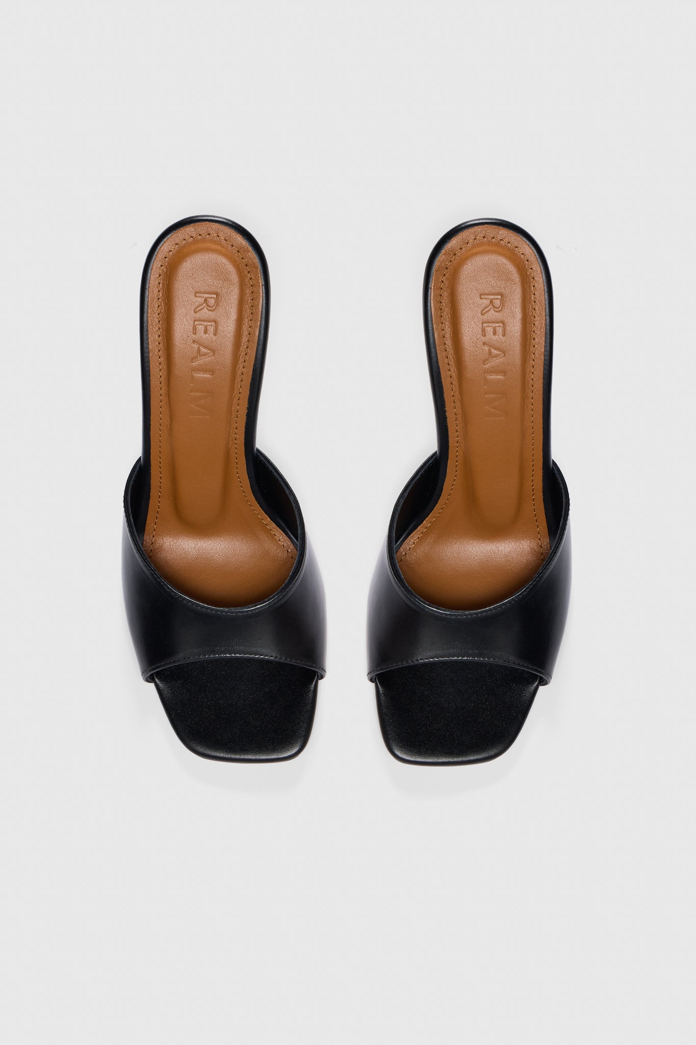 Black leather open-toe, slip-on heeled sandals with tan leather insoles embossed with Realm, shown from above on a plain white background.