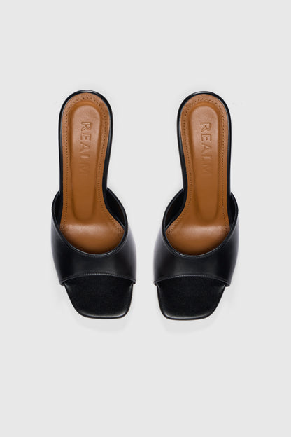 Black leather open-toe, slip-on heeled sandals with tan leather insoles embossed with Realm, shown from above on a plain white background.