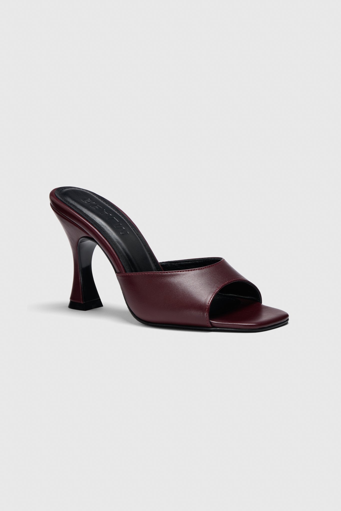 The Mules: a sleek burgundy leather slip-on with an open toe, square front, and flared black high heel on a plain light gray background.