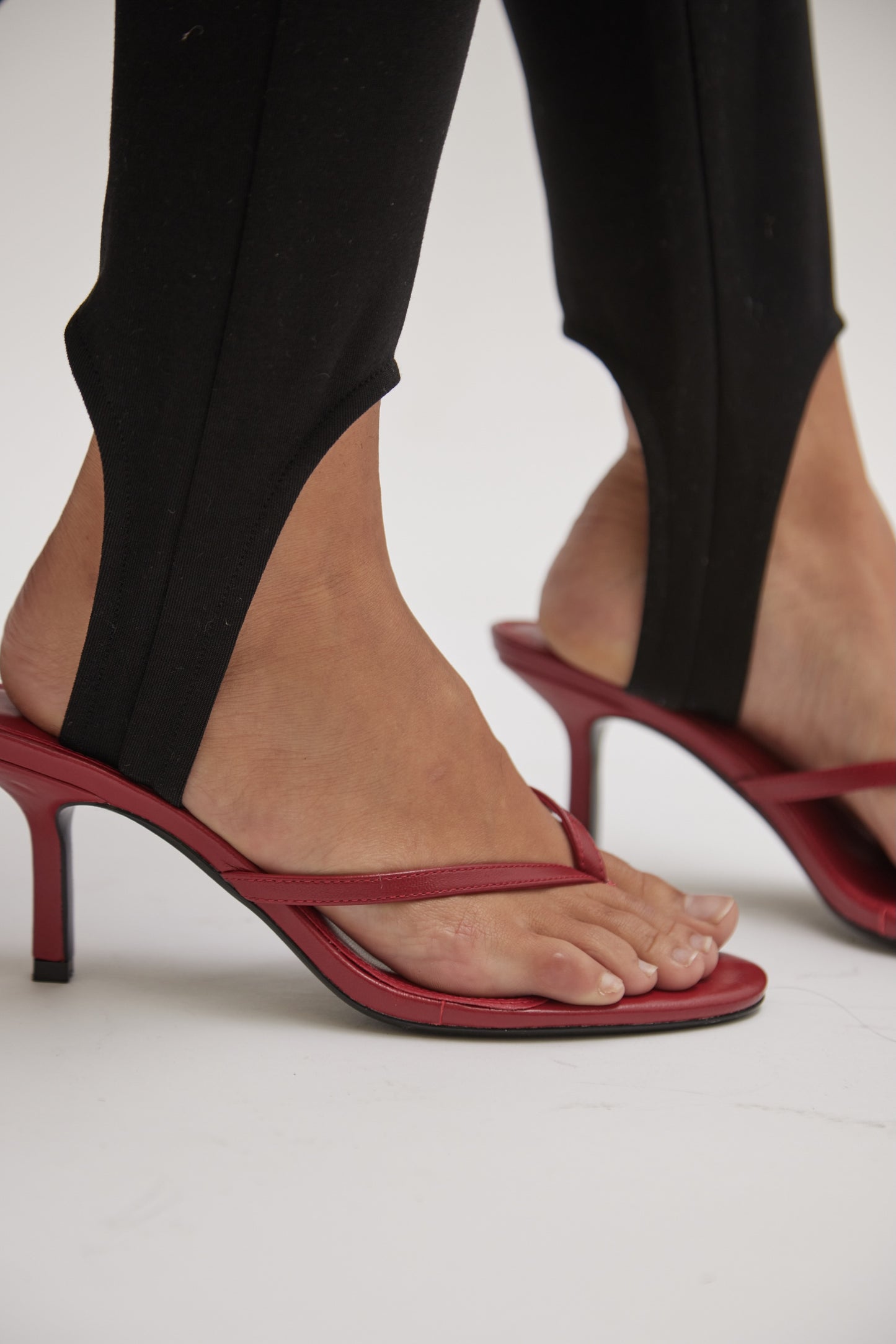 Close-up of a person wearing black stirrup pants and Spirit Heeled Sandals in red leather, highlighting their bare feet and toes.